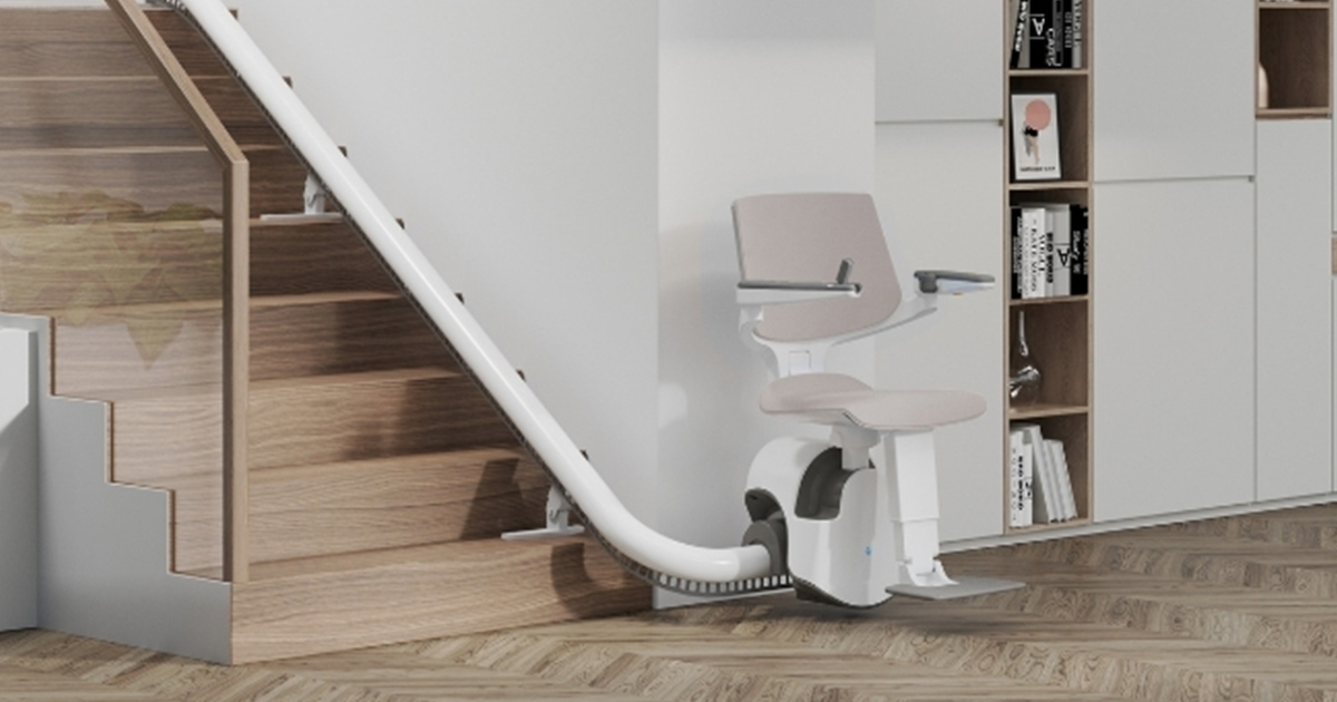 Nell'immagine è raffigurato un montascale rettilineo con una poltroncina di colore grigia: Il montascale presenta braccioli ergonomici e poggiapiedi regolabile